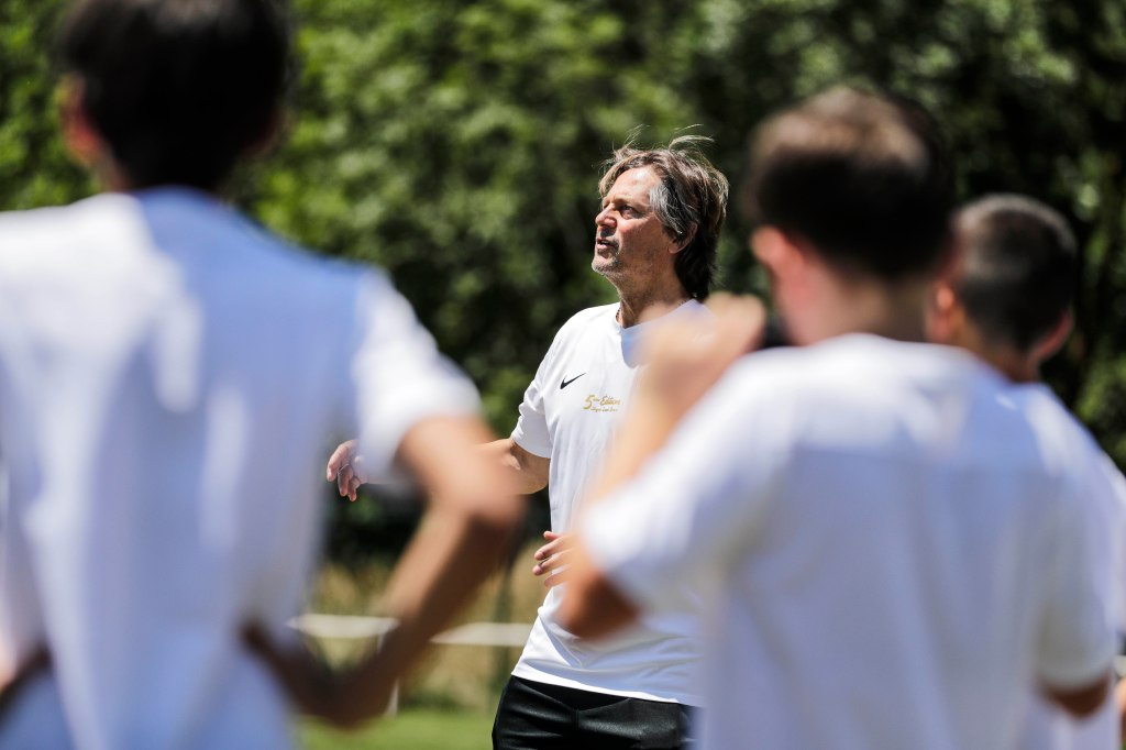 Alt text: A man in a white t-shirt and three other men wearing white t-shirts and black pants, possibly engaged in an outd...